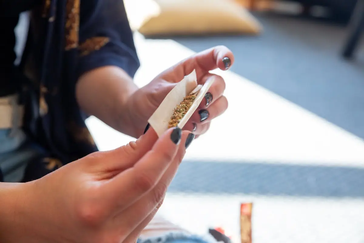 A close-up of a person rolling a cannabis joint indoors with natural light.