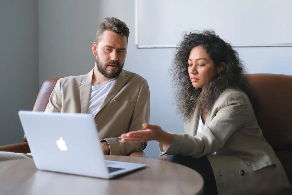 Serious colleagues in stylish outfits sitting at table and using laptop while discussing new project in office