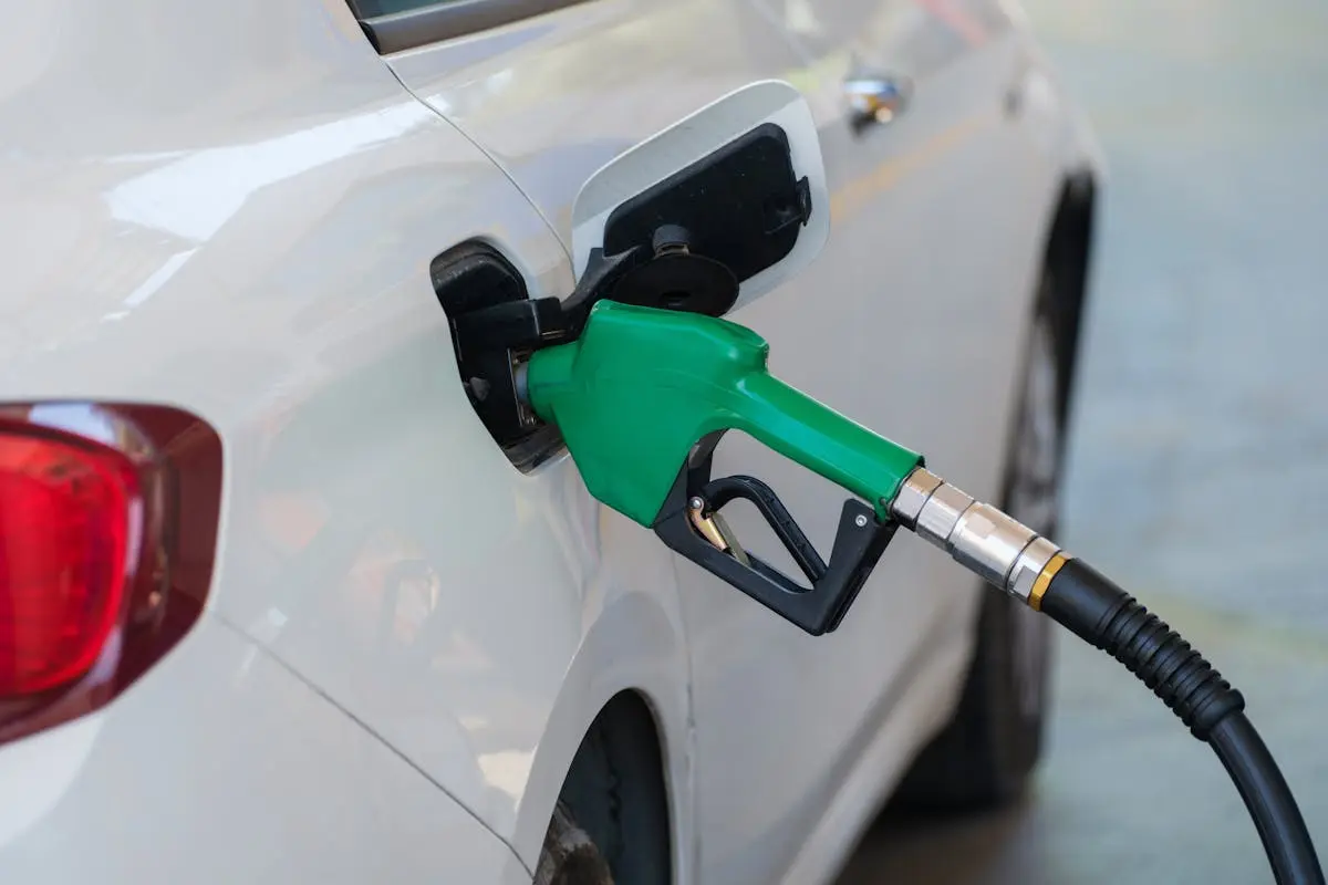 Close-up of a green nozzle refueling a white car at a gas station.