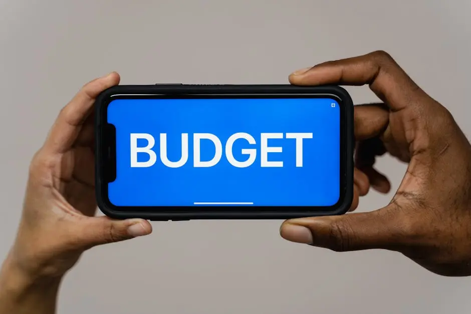 Two hands hold a smartphone displaying the word ‘budget’ on a blue screen, symbolizing financial planning.