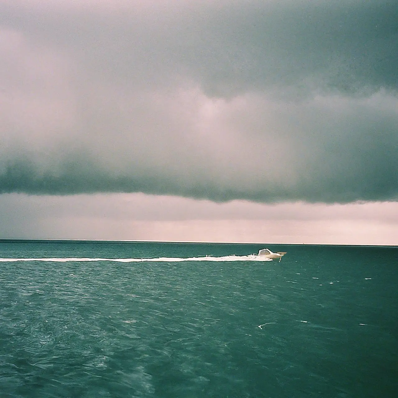 A small boat navigating through stormy seas toward calm waters. 35mm stock photo