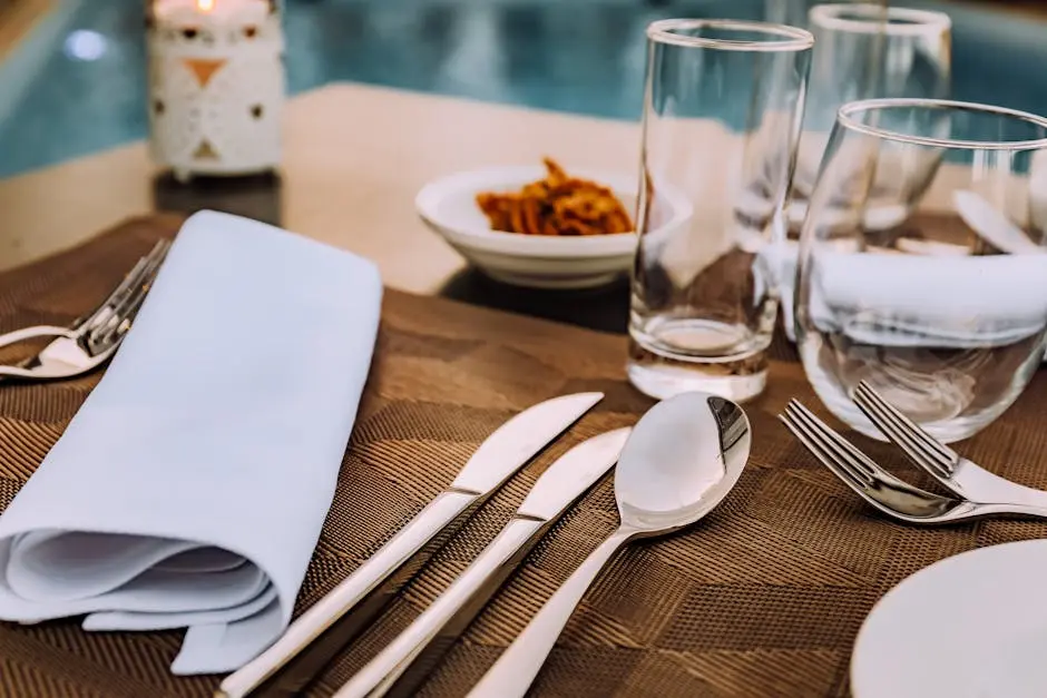 Sophisticated table setting with cutlery and glassware by a poolside, ideal for outdoor dining.