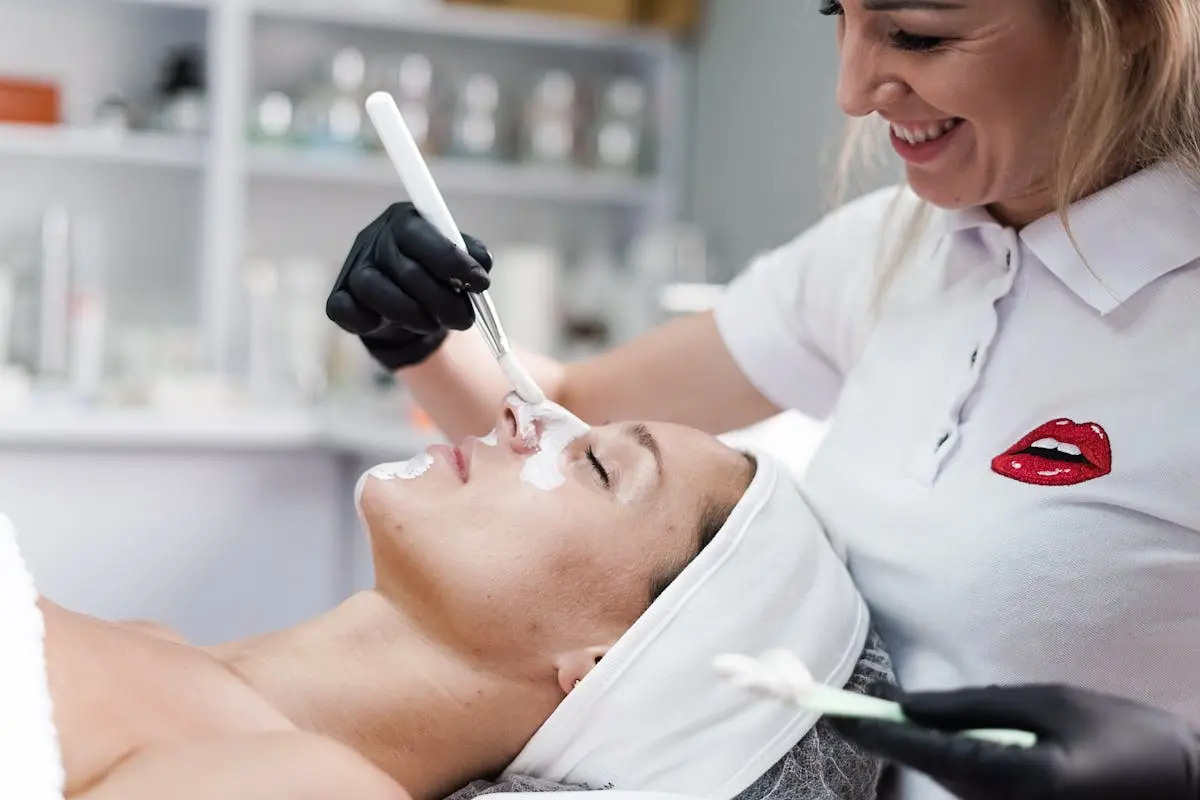 A beautician applying a face mask to a client in a salon, highlighting skincare and relaxation.