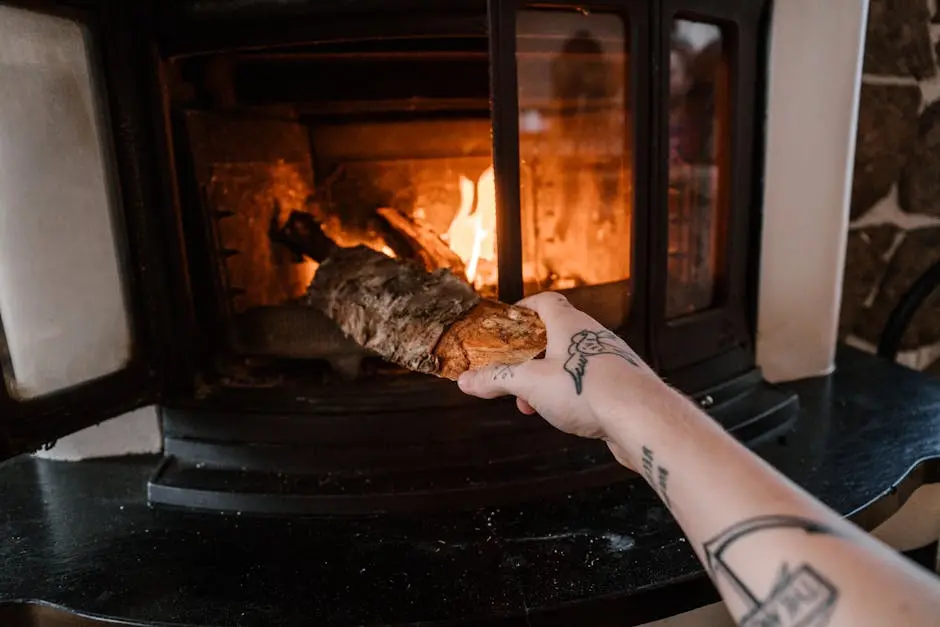 A tattooed hand placing a log into a roaring fireplace indoors.