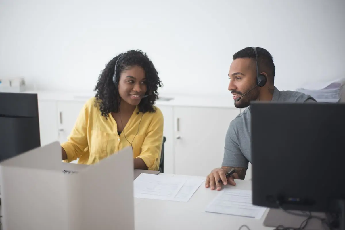 Woman in Yellow Dress Up Shirt with Headset Consulting to a Man Beside Her at Work