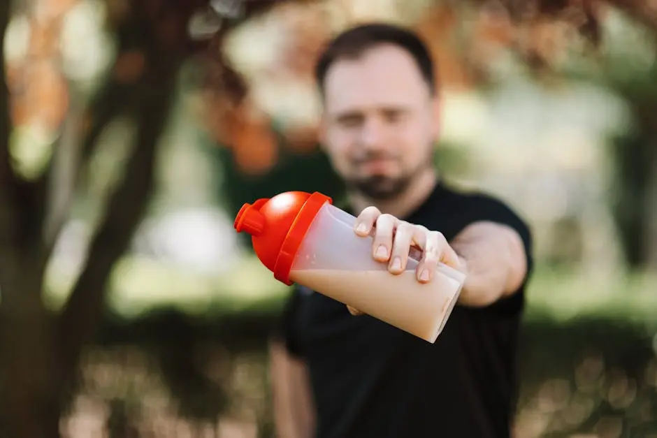 Man presenting a protein shake in a plastic tumbler against a blurred nature background.