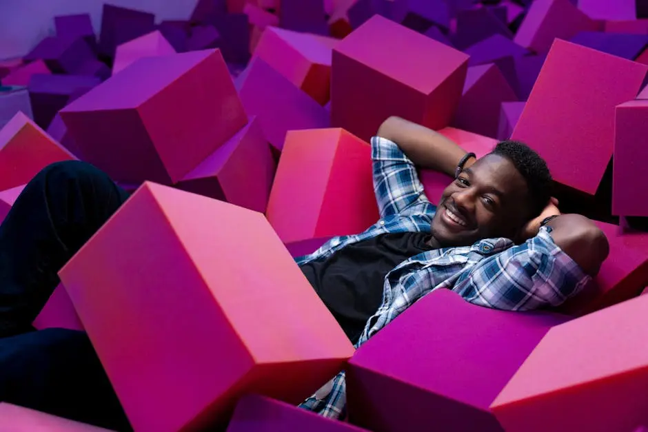 Smiling man lying among colorful foam blocks indoors. Fun and playful scene.