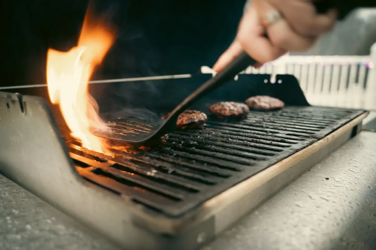 A person is cooking hamburgers on a grill