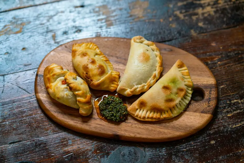 Appetizing baked empanadas served with chimichurri sauce on a wooden board. Perfect for food lovers.