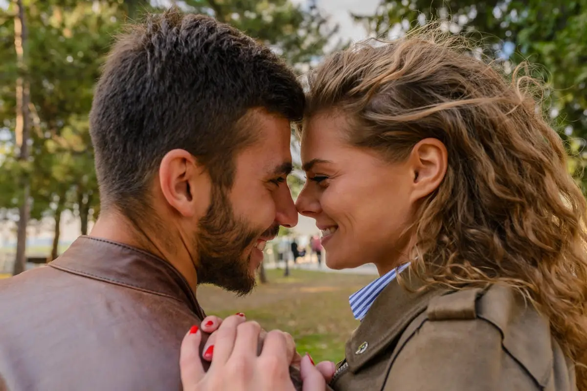 A young couple shares a tender moment face-to-face in a park, conveying warmth and affection.