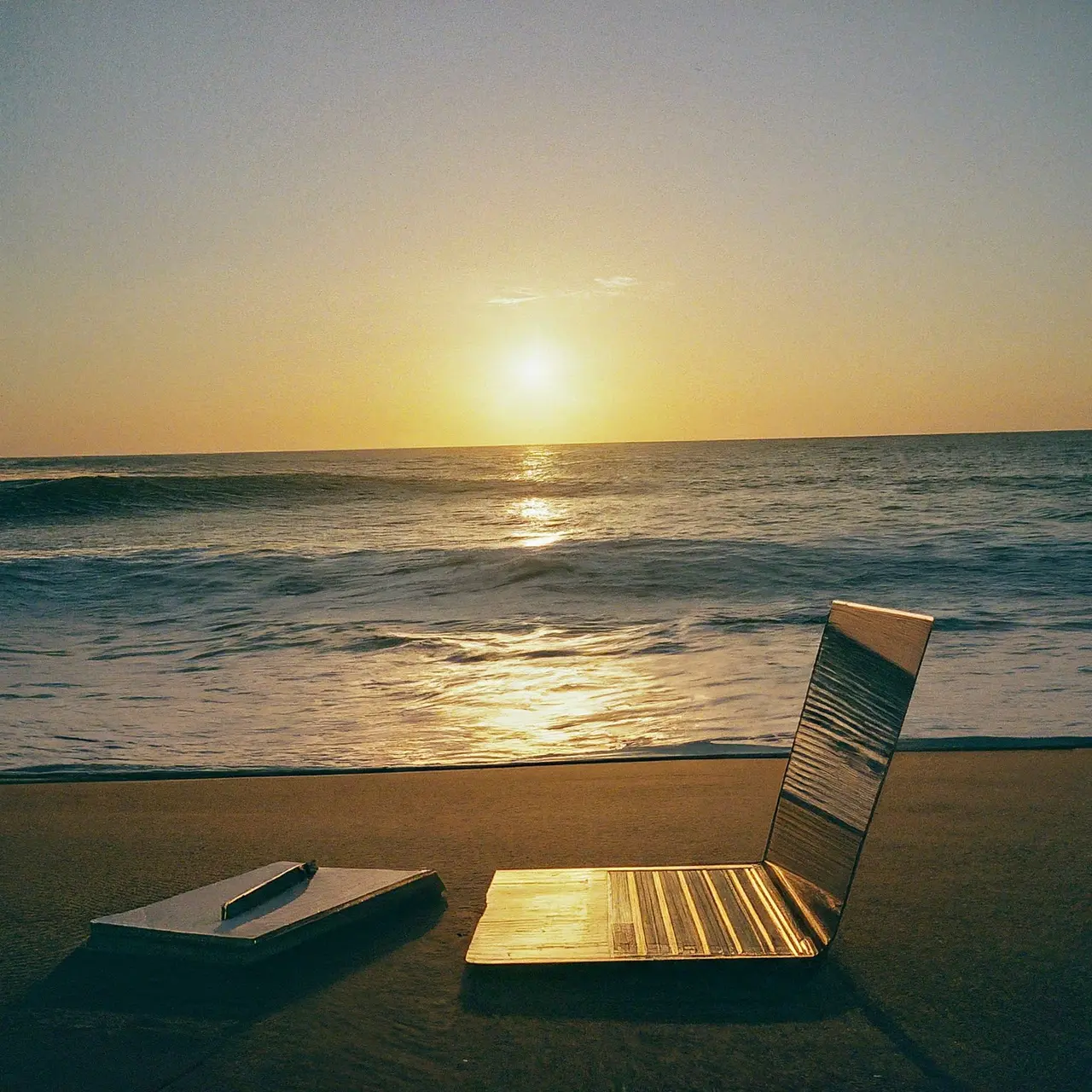 A serene beach at sunset with a laptop and notepad. 35mm stock photo