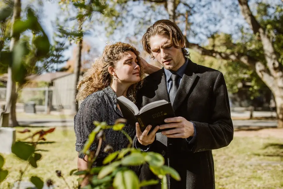 A grieving man and woman read the Bible together in a cemetery setting.