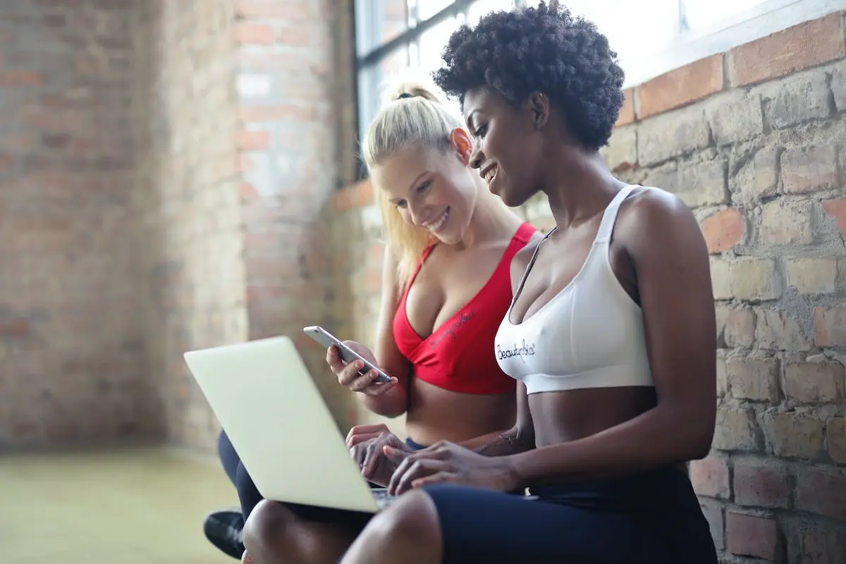 Two Women Wearing Red and White Sports Bras Sitting Near Brown Wall Bricks