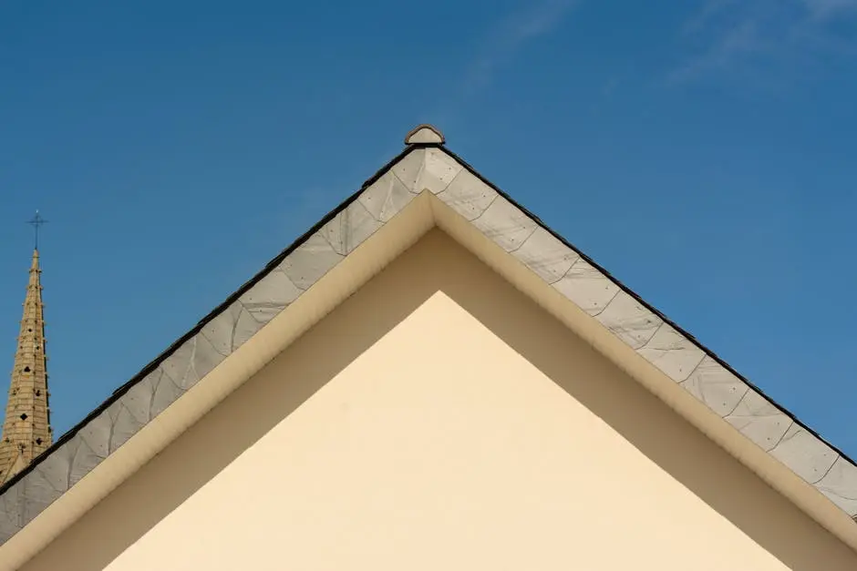 Minimalist architectural shot of building roof and church tower against clear sky.