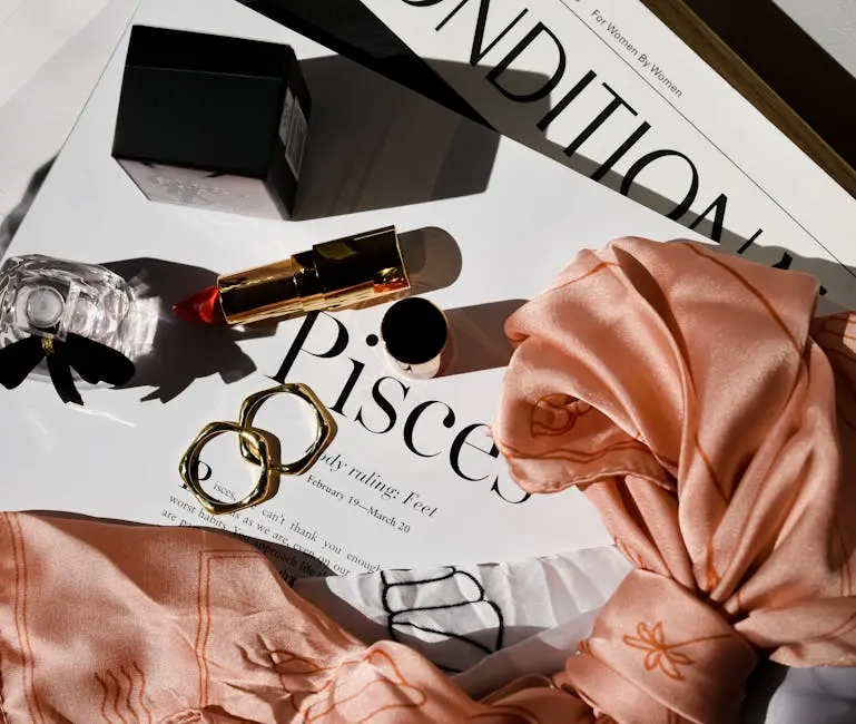 Chic flat lay featuring gold rings, red lipstick, perfume, and a stylish scarf over a fashionable magazine.