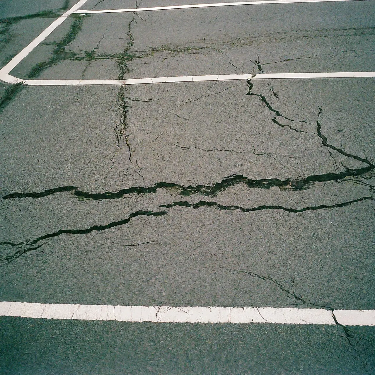 A cracked and worn asphalt parking lot with faded lines. 35mm stock photo