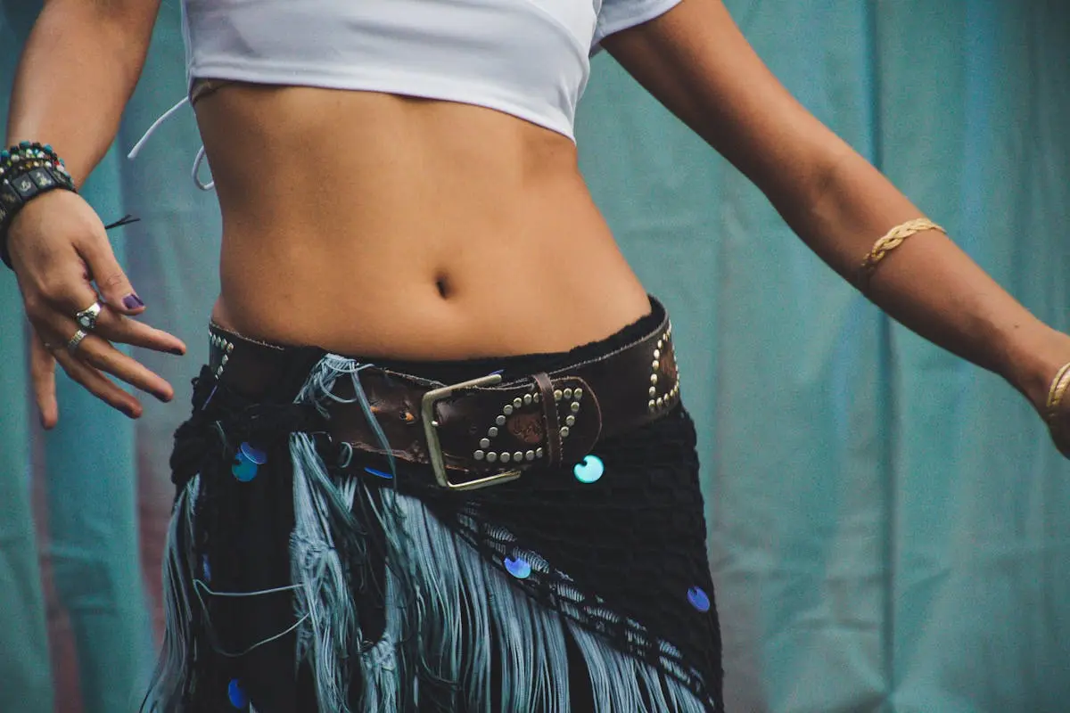 Close-up of a woman’s belly with stylish jewelry and bohemian attire in a dance pose.