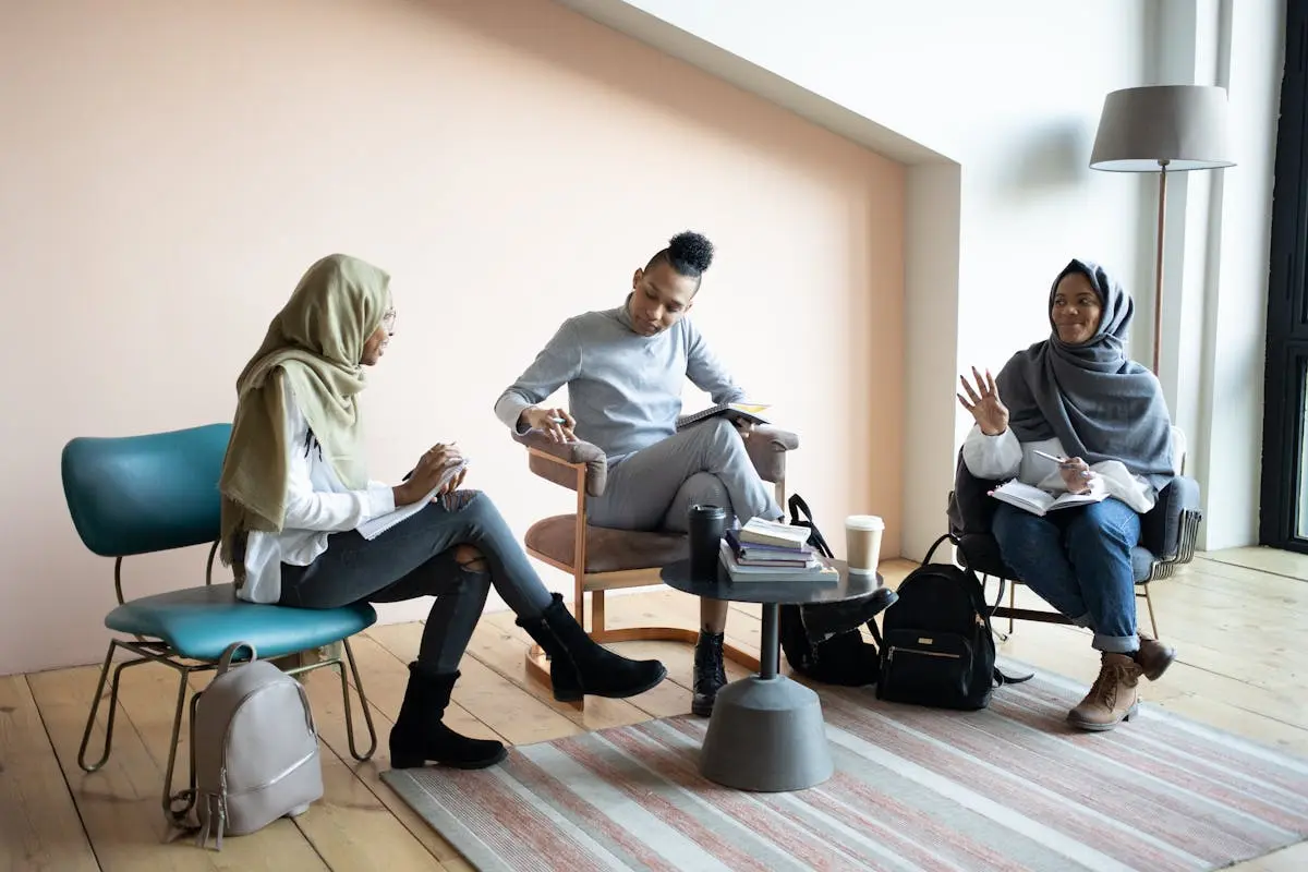 Full length positive young multiracial coworkers in casual outfits gathering in light coworking space and discussing business project together