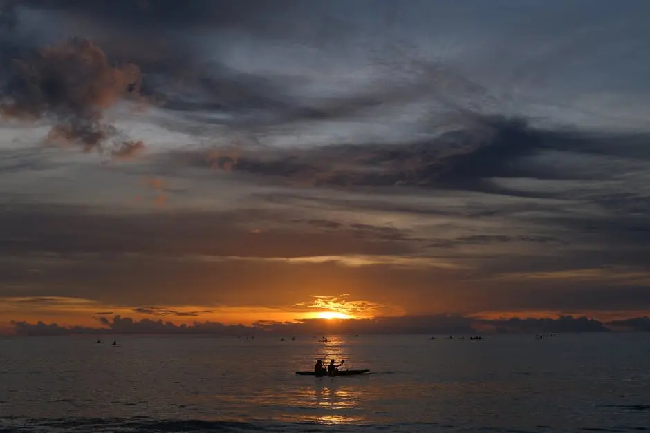 Serene ocean sunset with silhouette of boat and people on a calm evening.