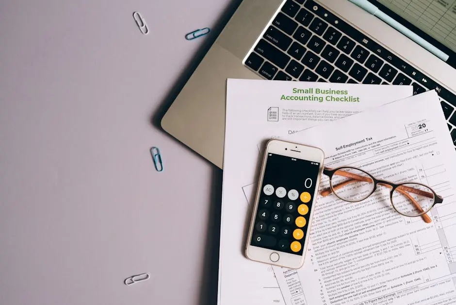 Flat lay of small business accounting tools including tax form, phone, and glasses on a desk.