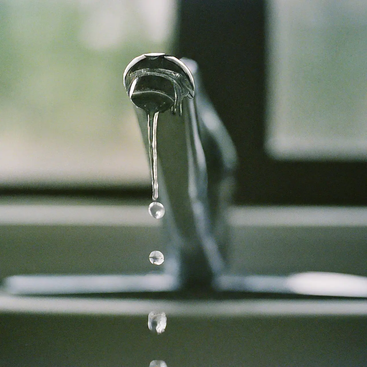 A close-up of a dripping faucet with water droplets. 35mm stock photo