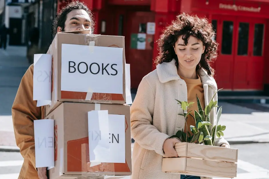 A joyful couple carrying boxes and plants while moving into a new home in an urban setting.