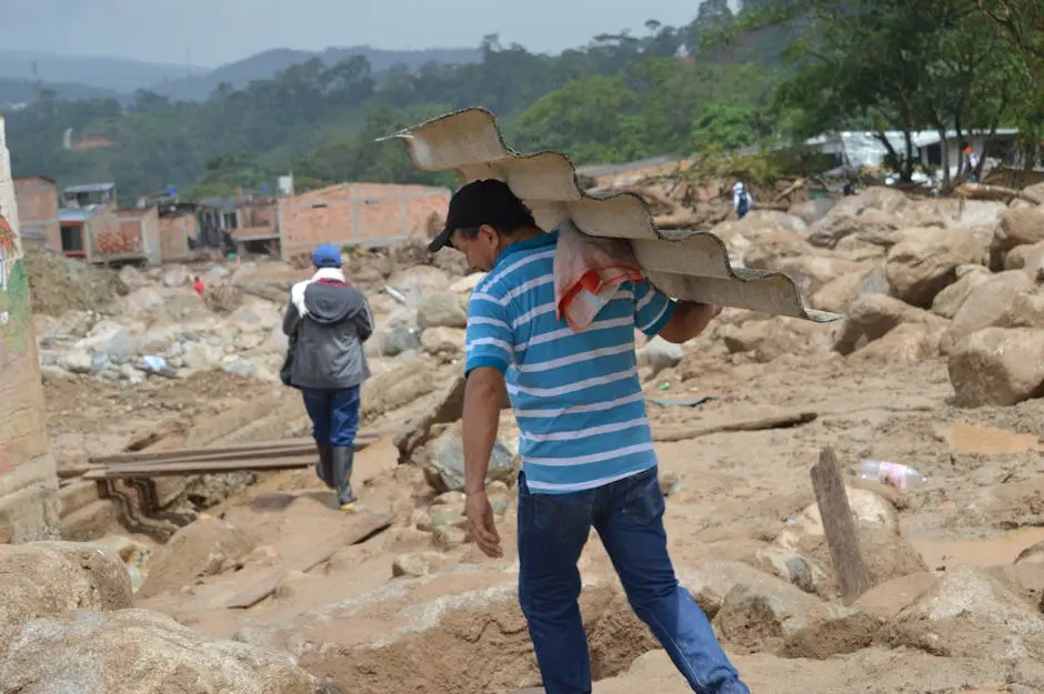 A man carries roofing material in a flood-affected area, showing resilience amidst destruction.