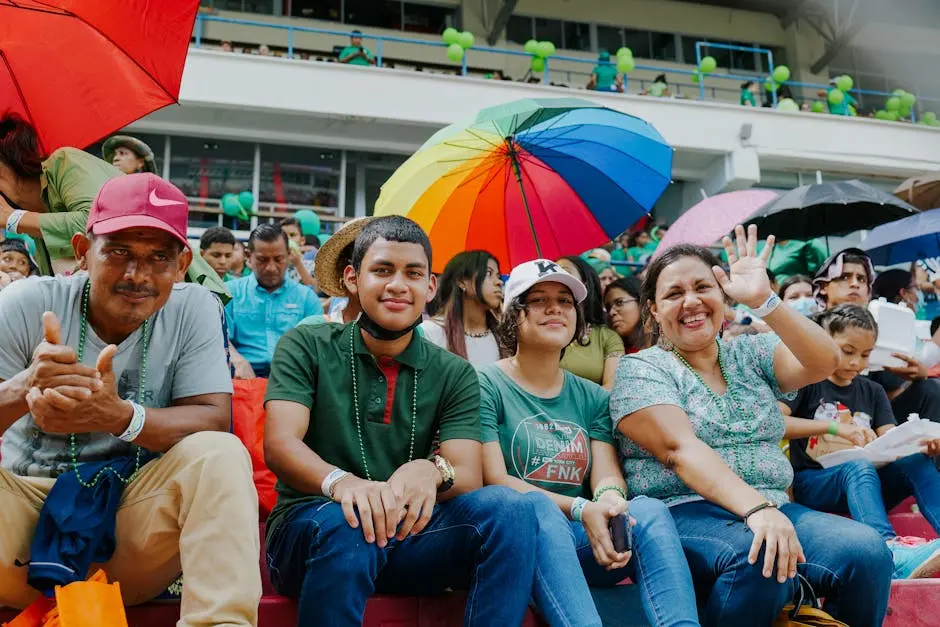 A diverse group enjoys a lively day at an outdoor stadium event with colorful umbrellas.