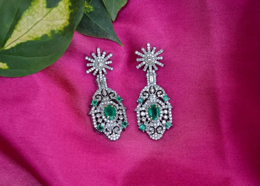 Close-up of intricate silver earrings with emerald stones on a vibrant pink fabric.