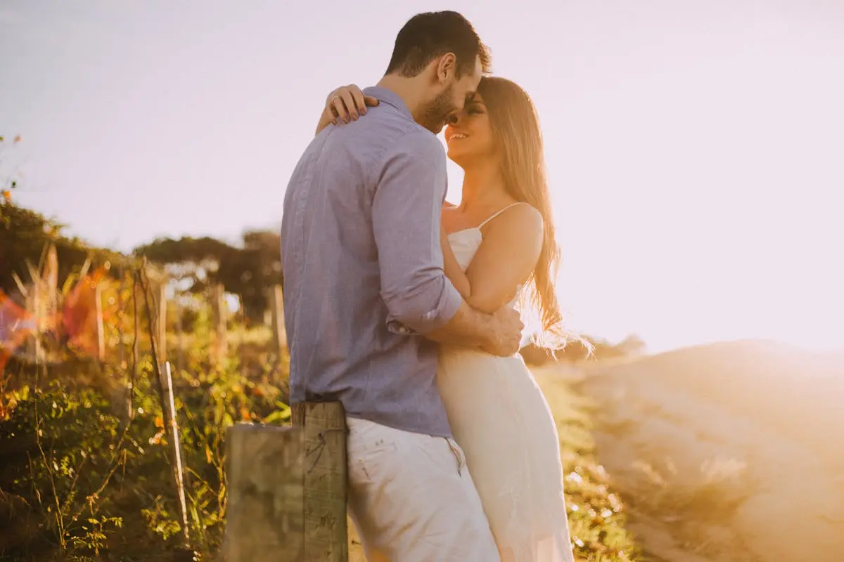 A couple shares a romantic moment embracing at sunset outdoors with warm light.