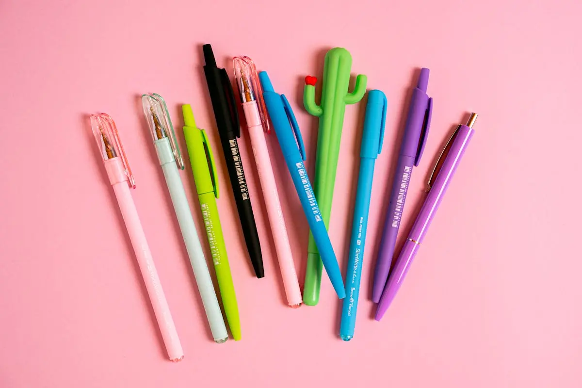 Collection of colorful pens arranged on a pink surface, showcasing vibrant stationery.