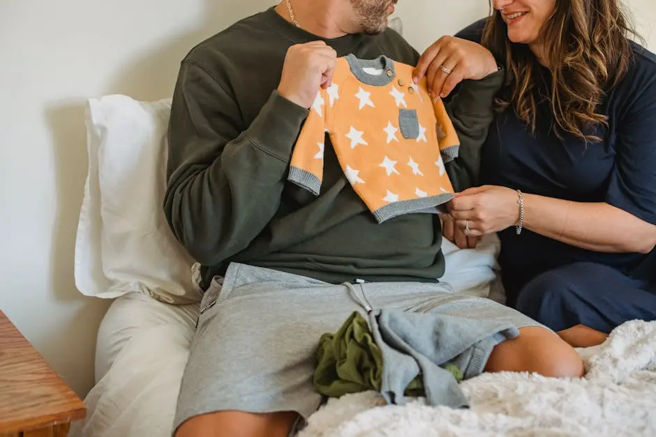 Crop faceless couple considering new apparel for newborn baby while resting on soft bed