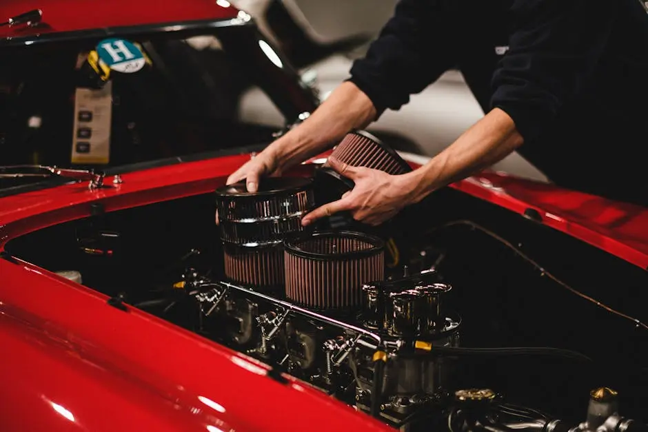 Close-up of a mechanic installing air filters on a classic red car’s engine inside a garage.