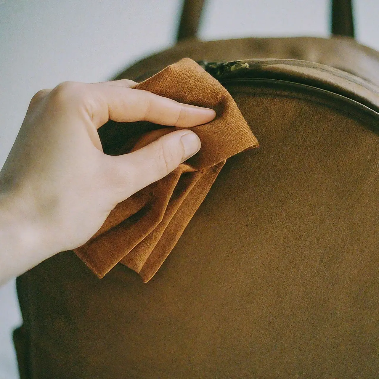 A hand gently cleaning a leather backpack with a cloth. 35mm stock photo