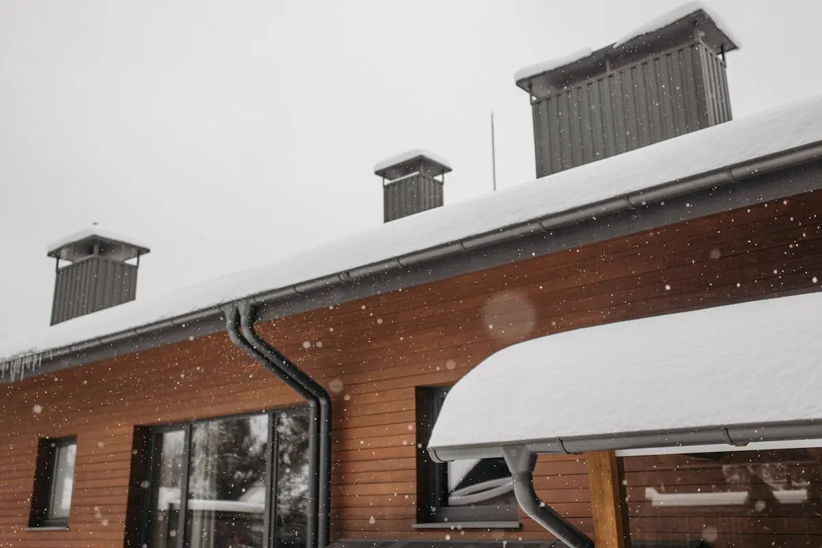 A close-up of a snow-covered roof with chimneys during winter snowfall, highlighting winter architecture.