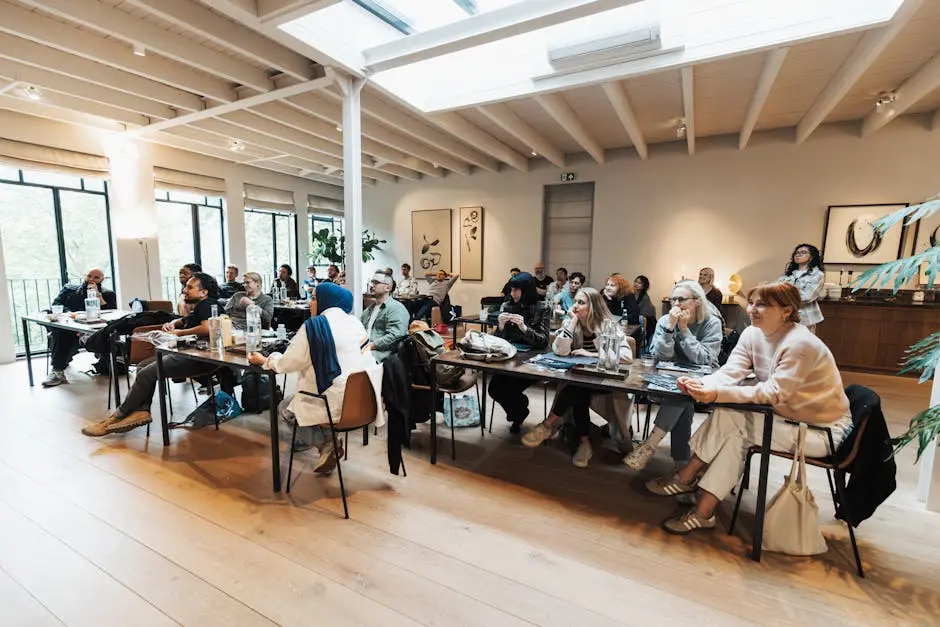 A large diverse group of adults engaged in an indoor seminar, seated and listening attentively.